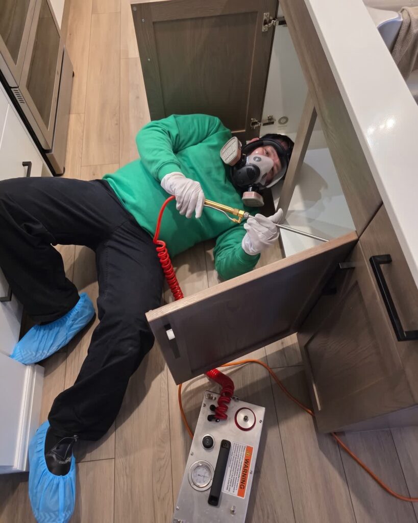 Technician in a respirator setting up heat treatment equipment inside a kitchen cabinet